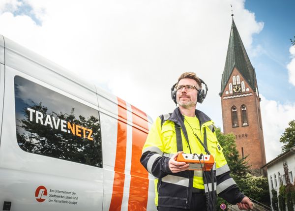 Monteure steht vor TraveNetz Auto und hat einen Gehörschutz auf